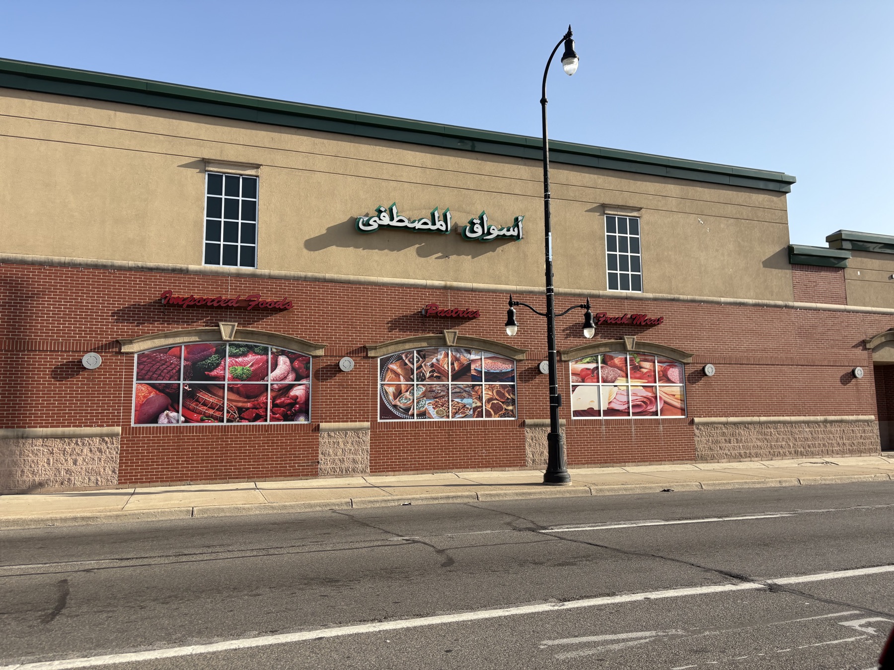 A market fascia in Dearborn lettered only in Arabic, above English signs reading Imported Foods, Pastries and Fresh Meat.